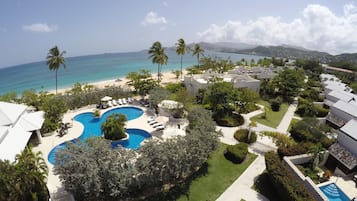 A resort with a large swimming pool, palm trees, and a view of the ocean.
