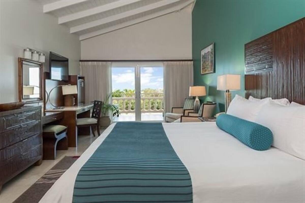 A hotel room with a bed, desk, chairs, and a view of the outdoors.