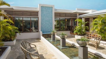 A modern outdoor area with stone flooring, a central water feature, and seating areas with planters.