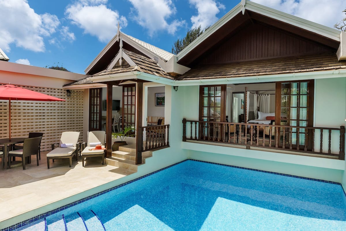 A poolside area with a covered seating area, a pool, and a building with large windows and a balcony.