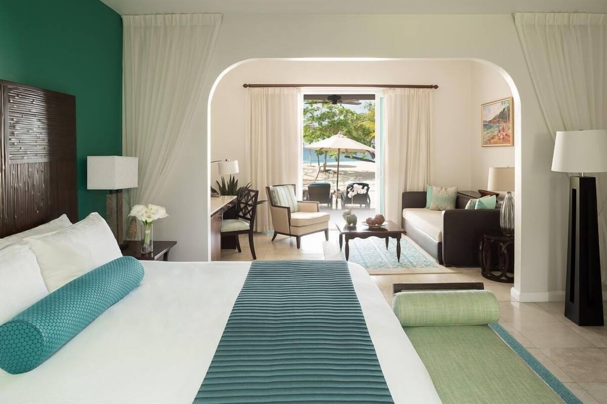 A hotel room with a bed, a sofa, a chair, a table, and a view of the outdoor area.