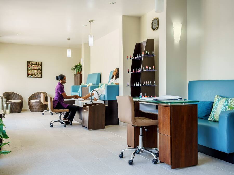 Un salón moderno con una zona de recepción, un sofá azul y una barra con esmalte de uñas.