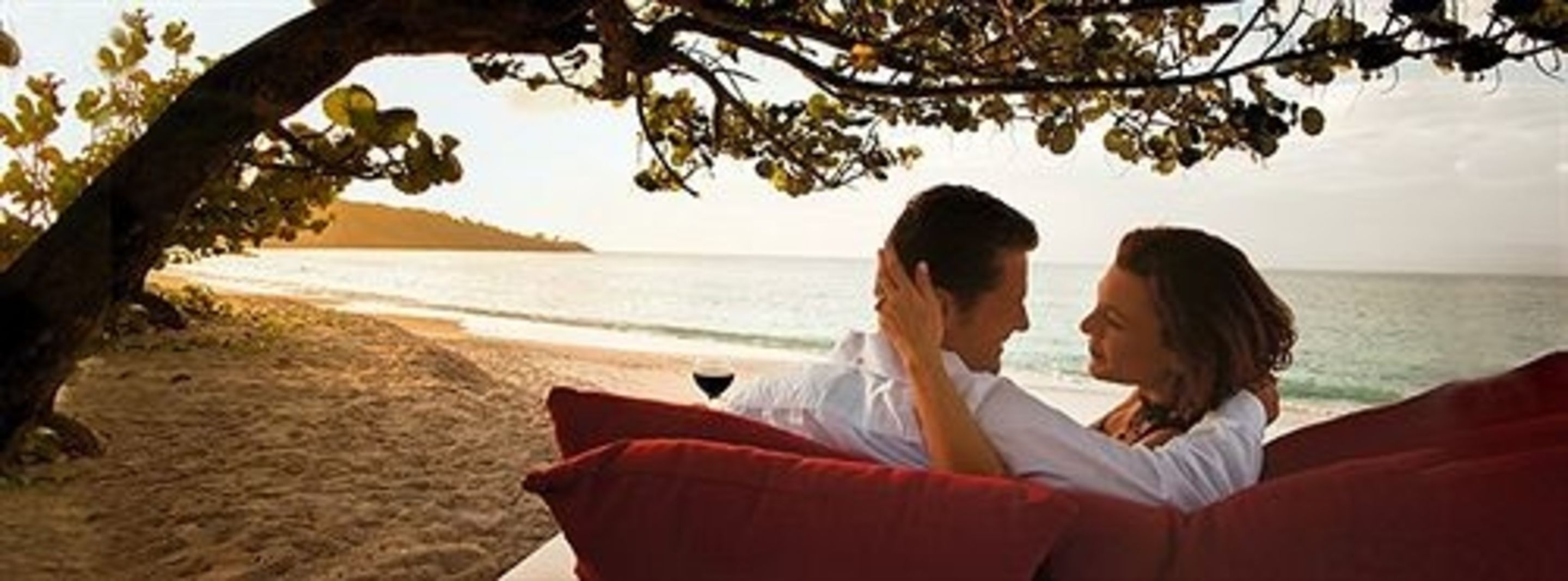 A couple sitting on a red couch by a beach with a view of the ocean and a sandy shore.