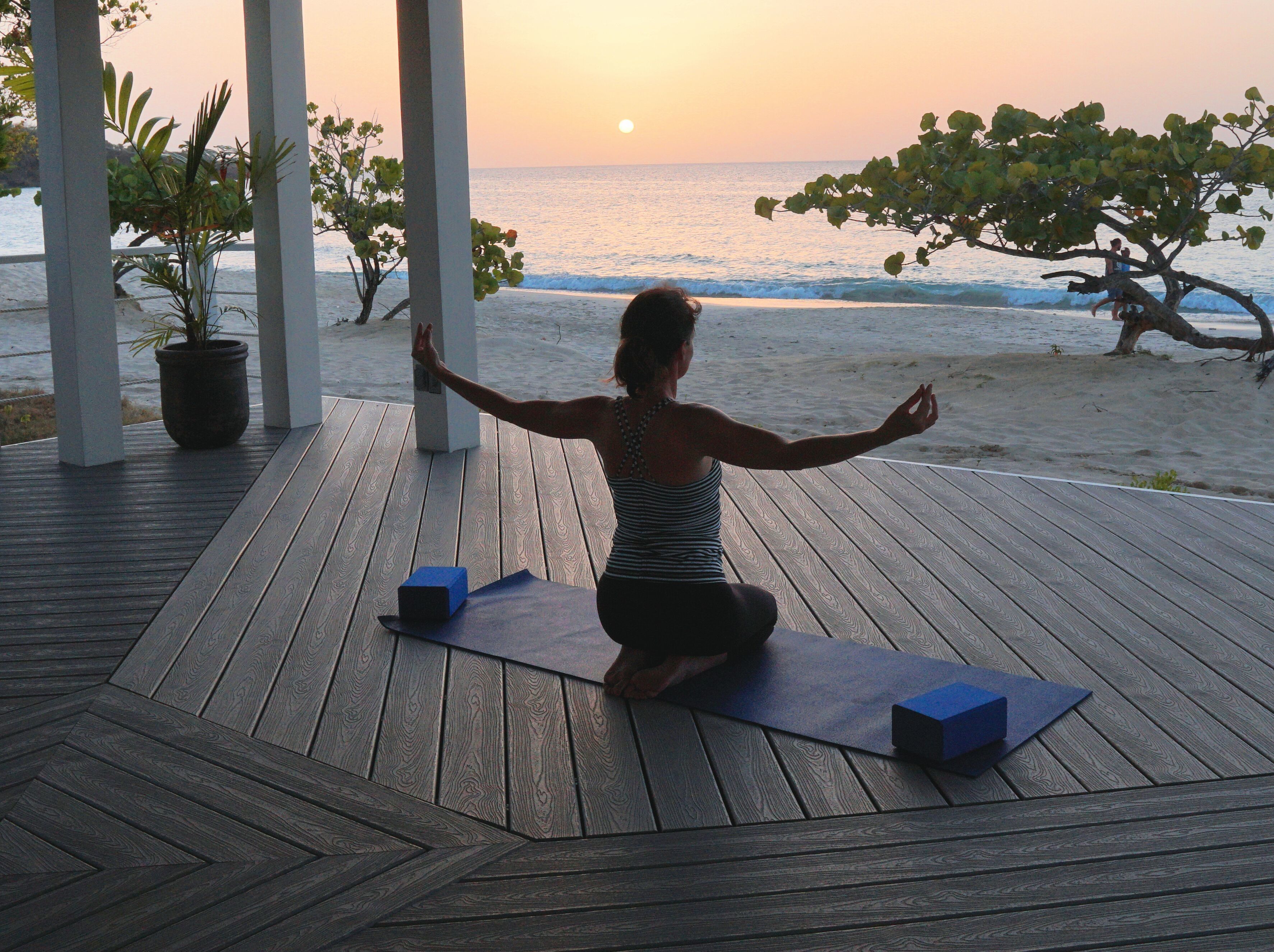 A person practicing yoga on a wooden deck with a view of the ocean at sunset.