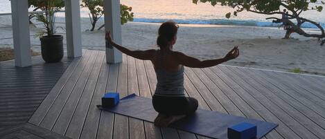 A person practicing yoga on a wooden deck with a view of the ocean at sunset.