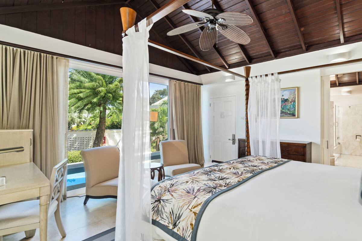 A bedroom with a bed, a desk, a chair, a ceiling fan, and a view of the outdoors.