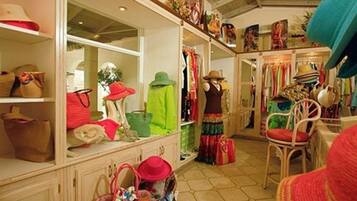 Une boutique élégante où l’on trouve des étagères remplies de chapeaux et de sacs, un mannequin portant une tenue colorée, et un fauteuil avec un coussin rouge.