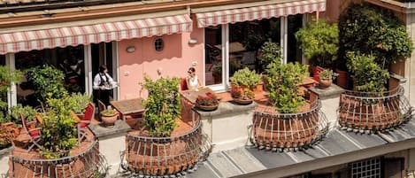 Una terraza en la azotea con plantas en macetas, mobiliario exterior y fachada de un edificio rosa.