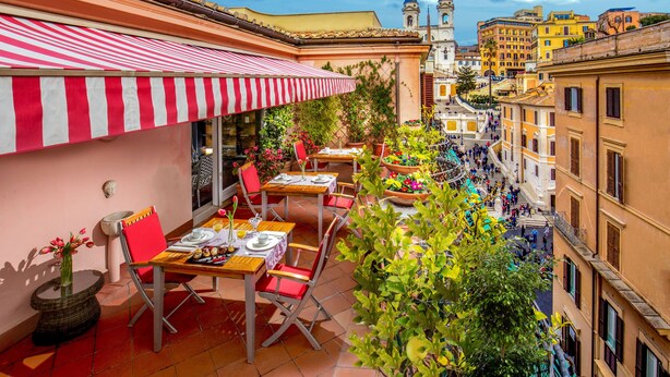 An outdoor café with red and white striped awnings, tables with chairs, and a view of a historic building with a bell tower. - The Inn at the Spanish Steps (Rome)
