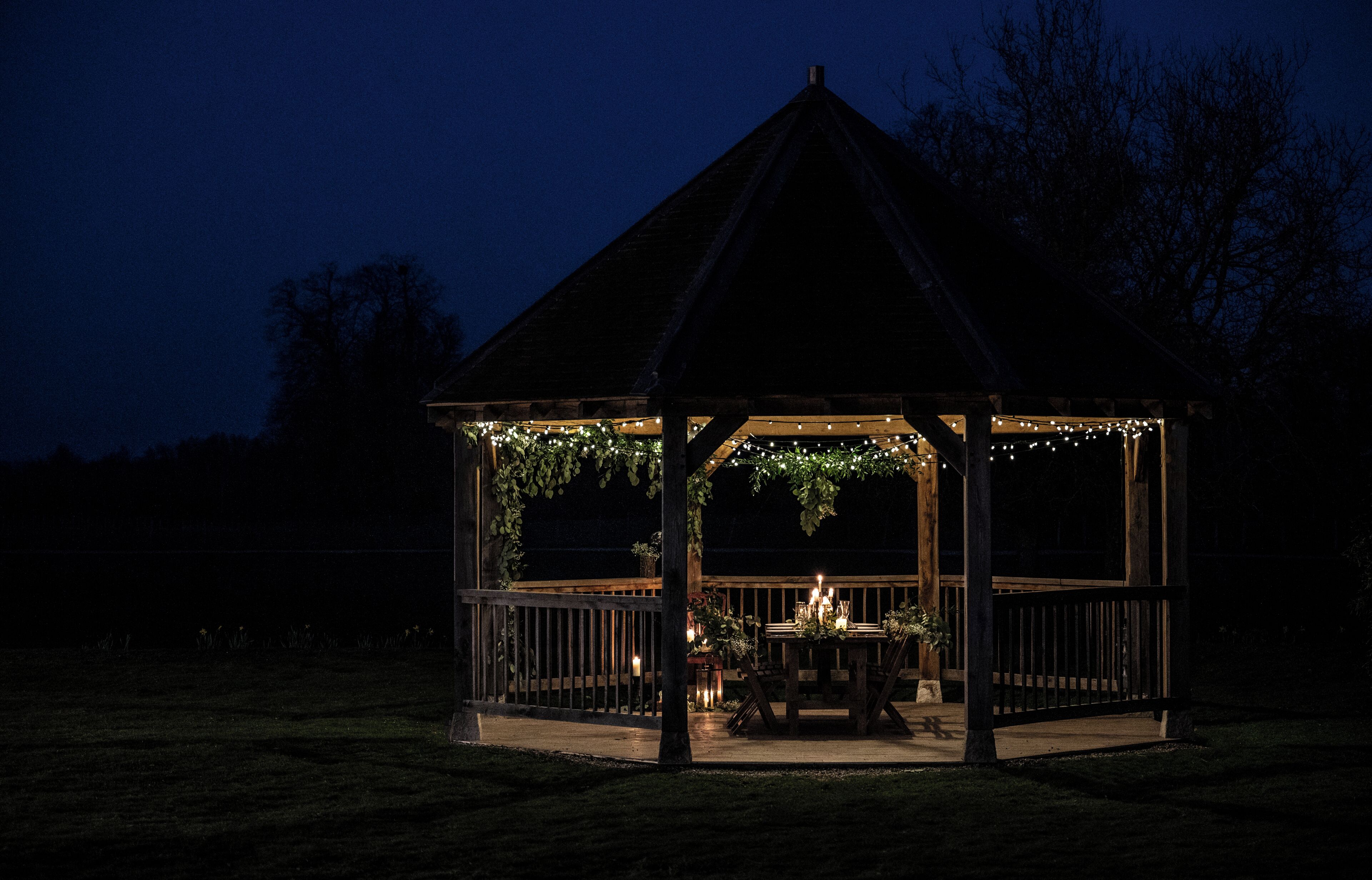 Een pergola met houten dak en leuning, versierd met lichtslingers en begroeiing.