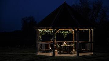 Een pergola met houten dak en leuning, versierd met lichtslingers en begroeiing.