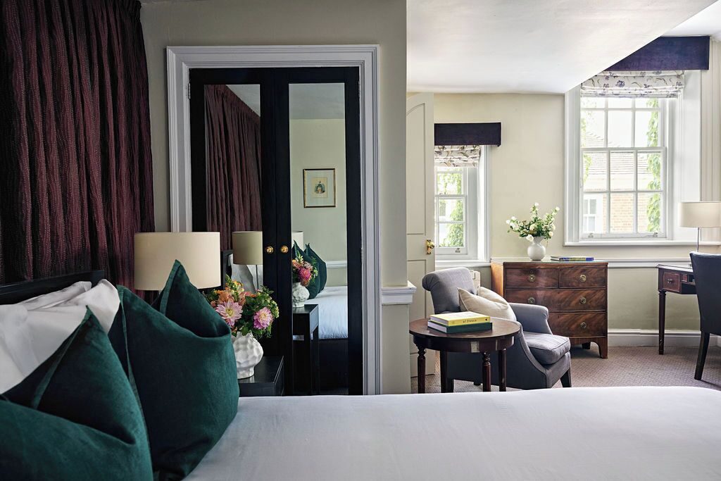 A hotel room with a bed, a desk, a chair, a dresser, and a door leading to another room.