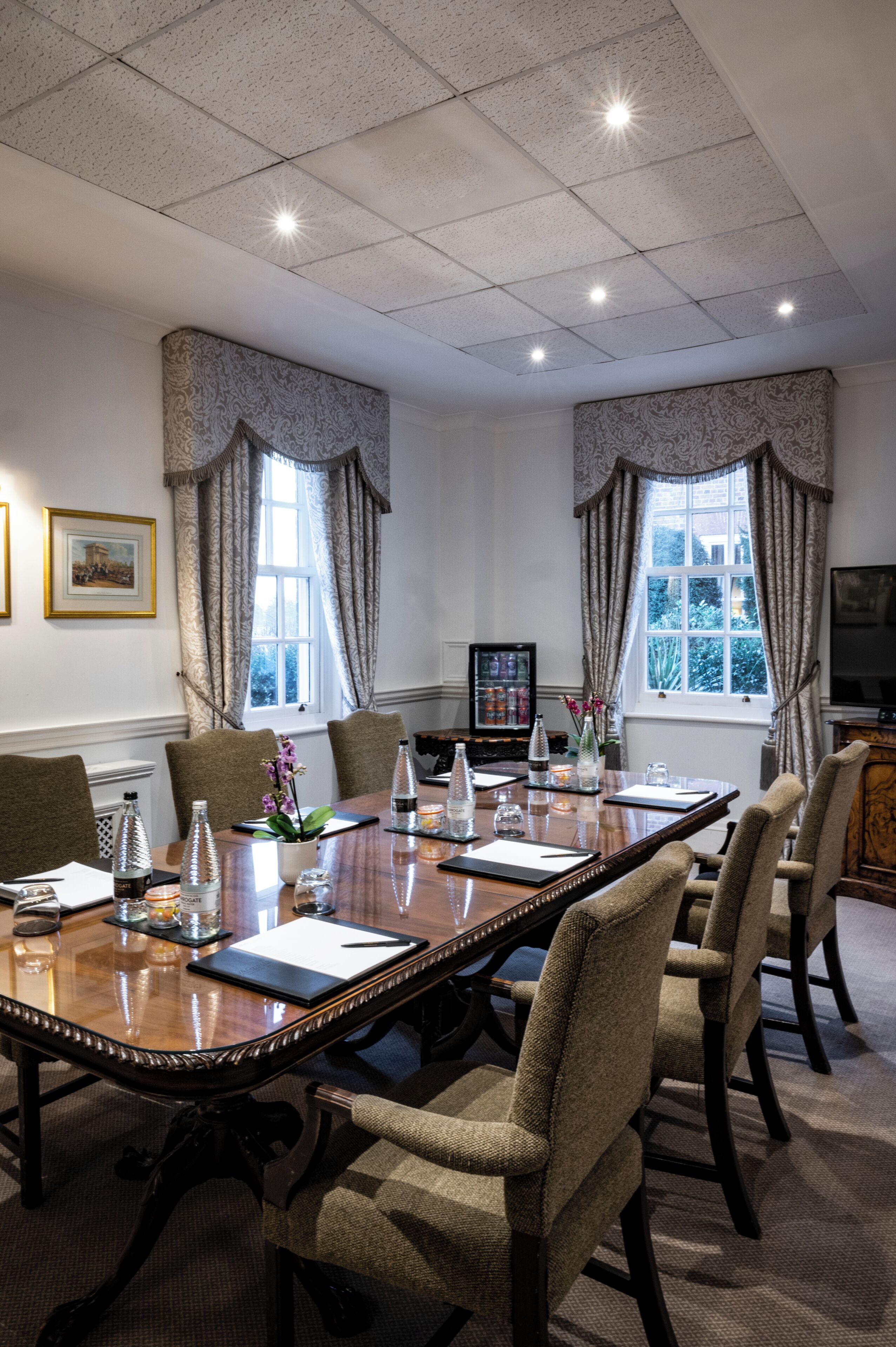 A conference room with a long table, chairs, a television, and framed pictures on the wall.