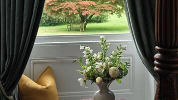 A room with a window, a vase with flowers, a round wooden table, and a yellow pillow.
