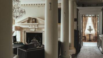 A grand hallway with classical architecture, including columns and a fireplace with a mantel.