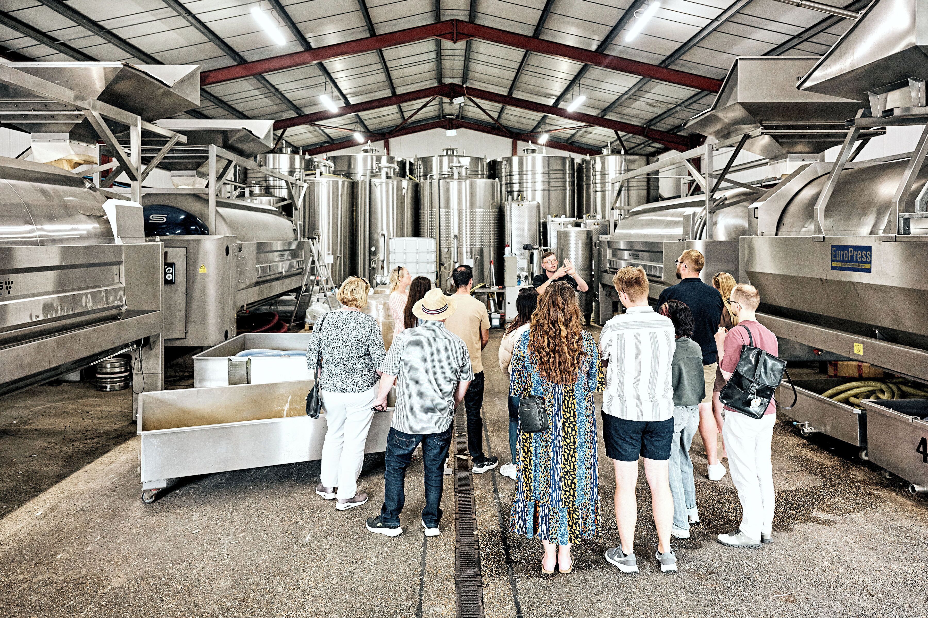A group of people in a large industrial facility with stainless steel tanks and machinery.