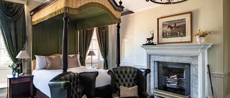 A four-poster bed with a canopy, a fireplace, a chandelier, and a framed picture on the wall.