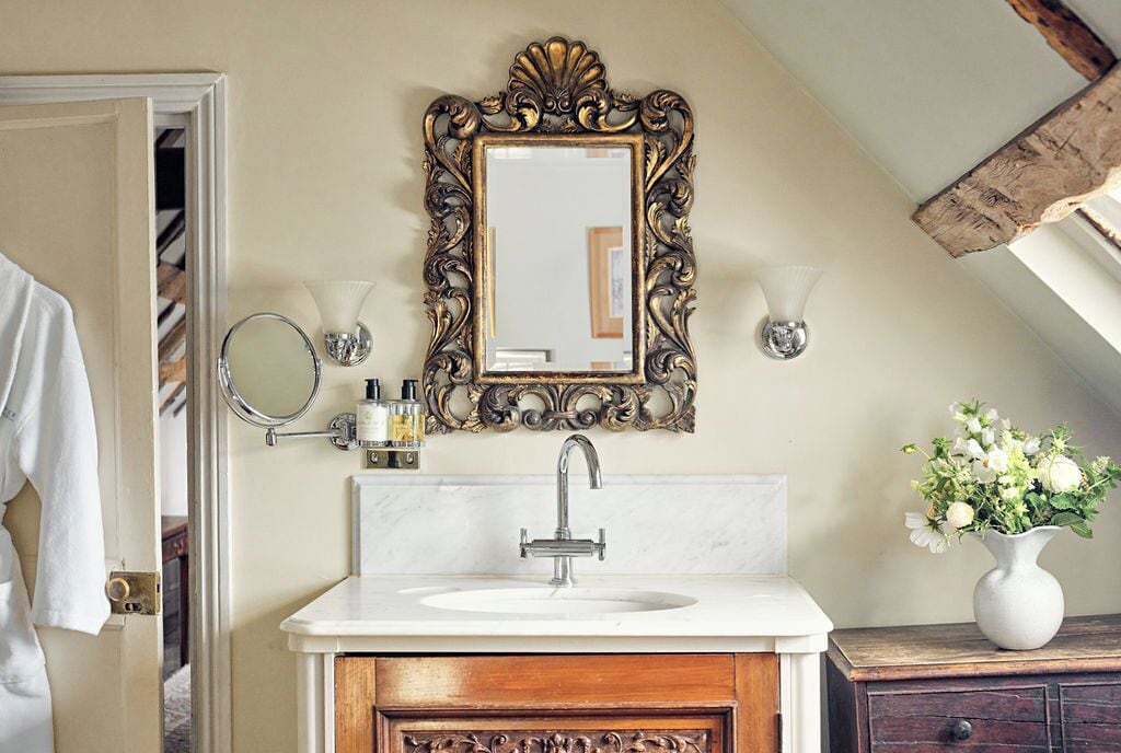 A bathroom with a white sink, ornate gold-framed mirror, and a wooden cabinet.