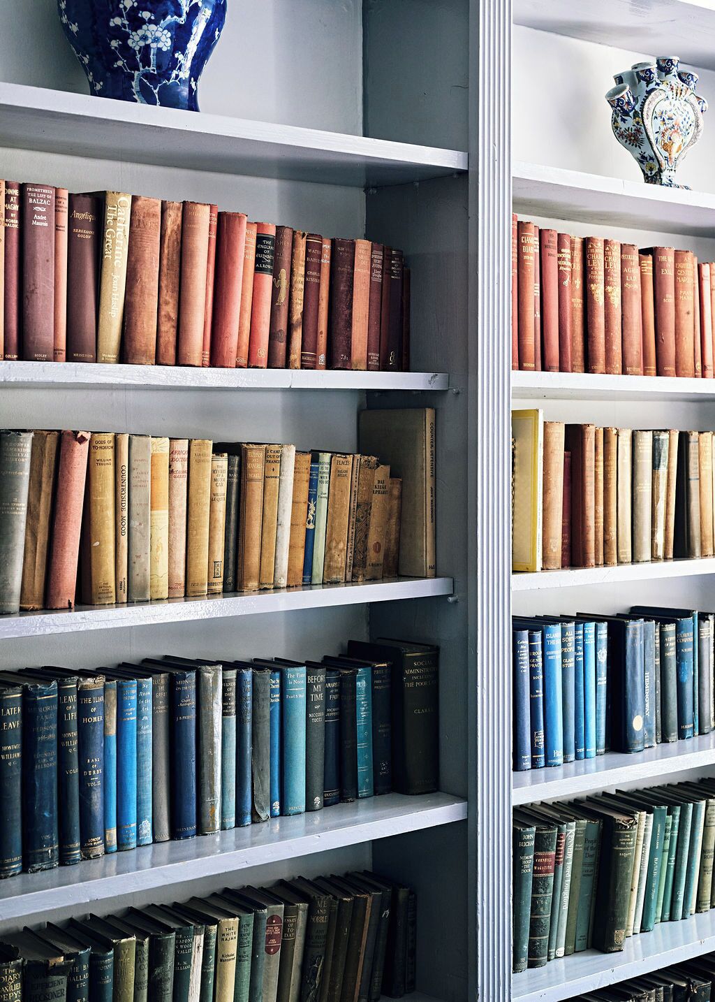 A bookshelf filled with various books, a blue vase, and a decorative ceramic piece.