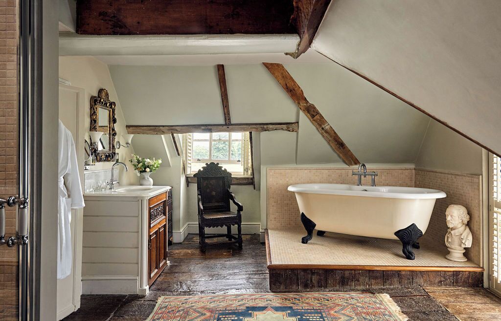 A rustic bathroom with a clawfoot tub, a wooden chair, and a small statue.