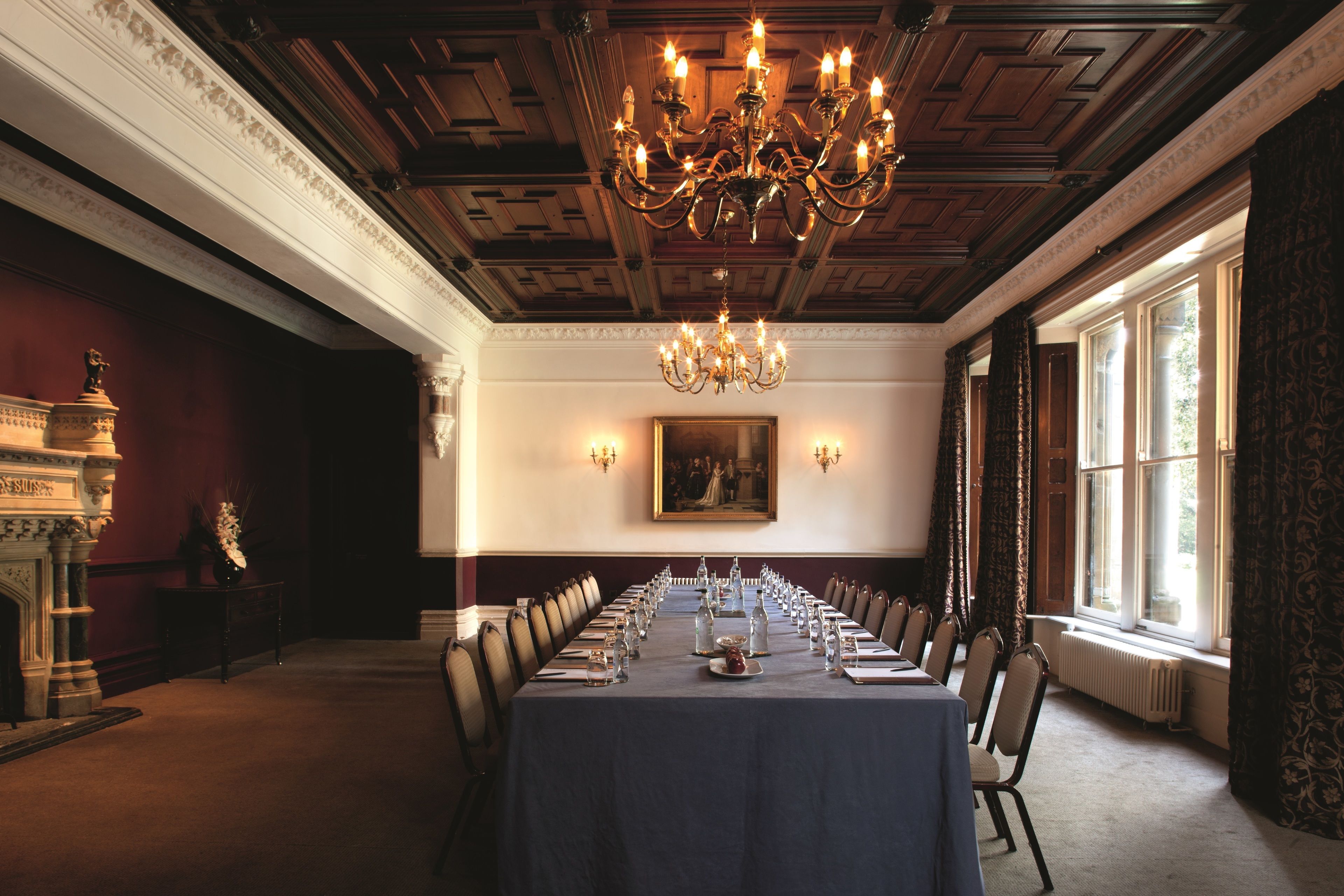 A formal dining room with a long table set for a meal, a chandelier, and a fireplace.