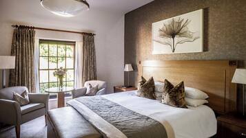 A hotel room with a large bed, a chair, a table, and a window with curtains.