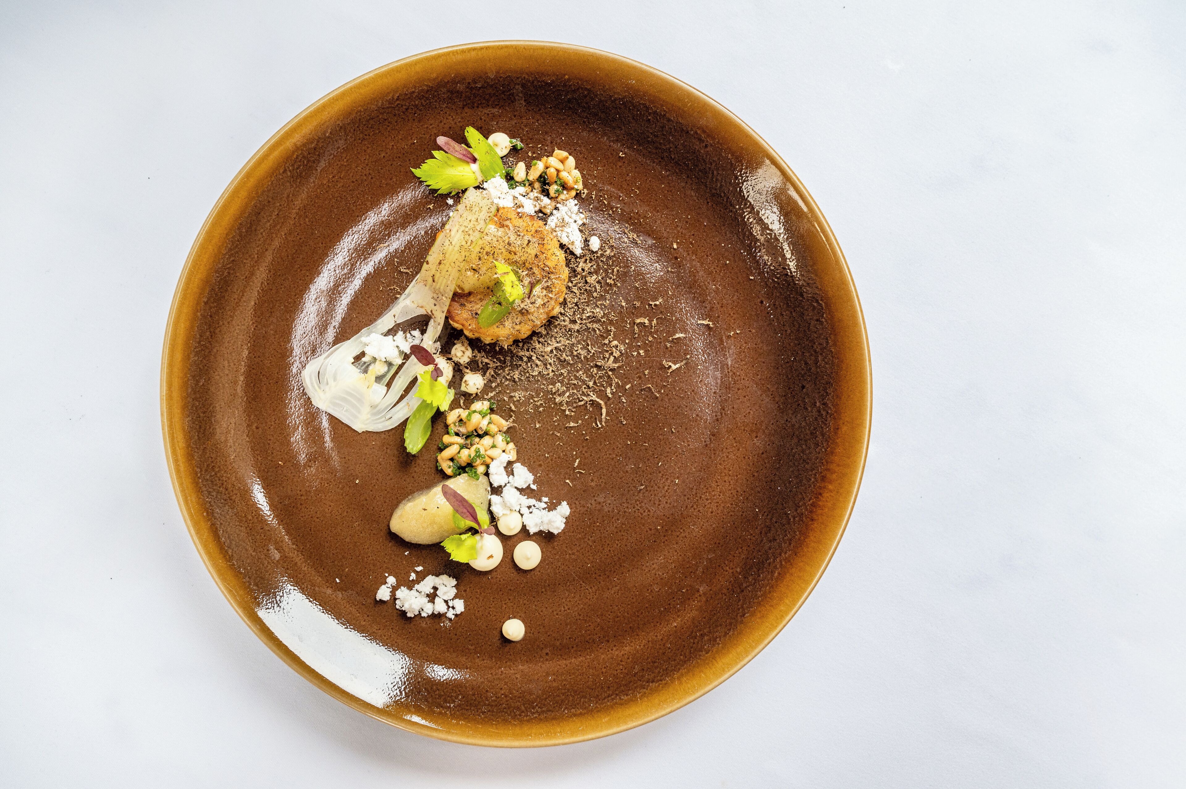 A brown ceramic plate with a food item, garnishes, and a fork.