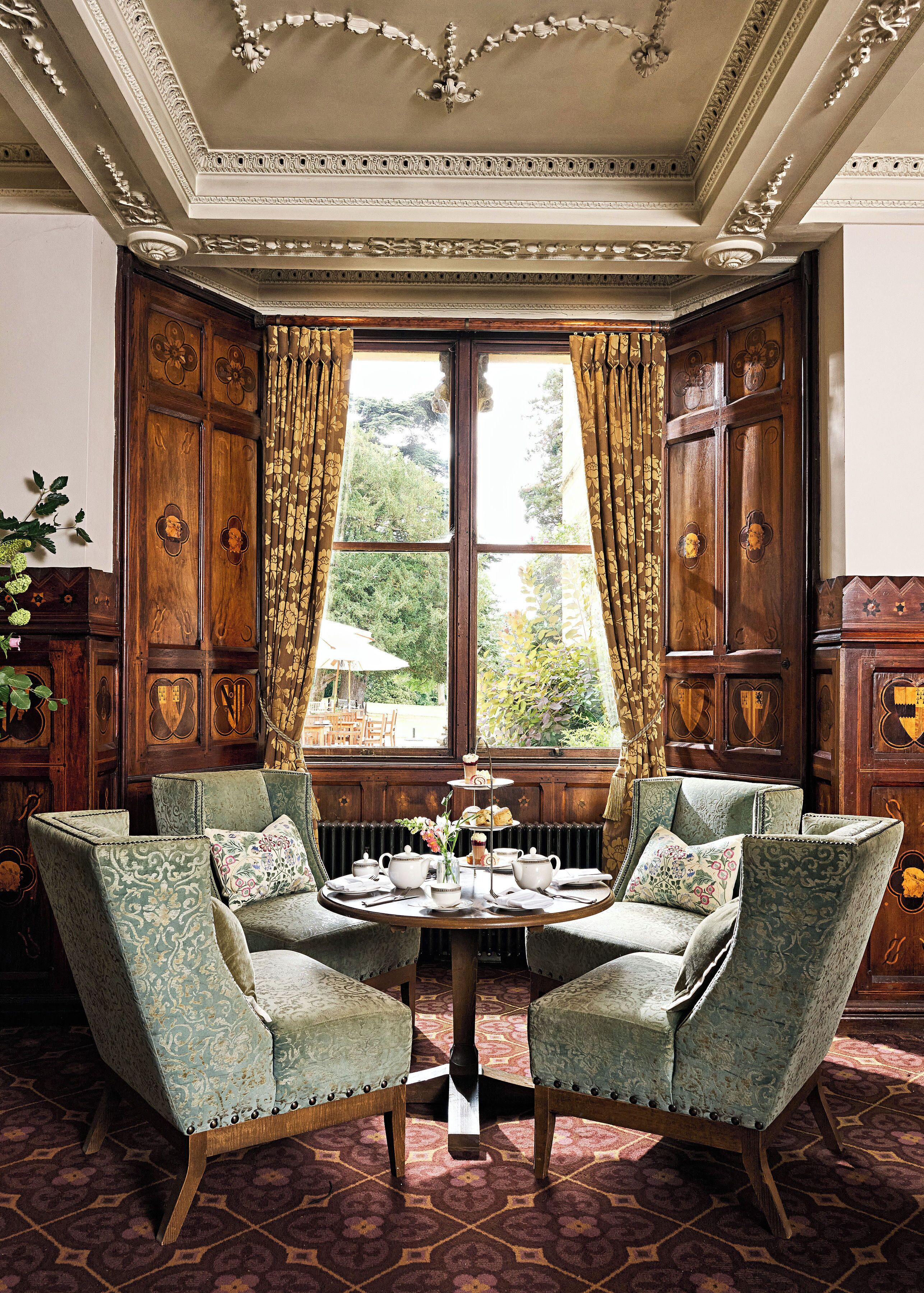 A room with a bay window, ornate wooden paneling, and a table set for tea.