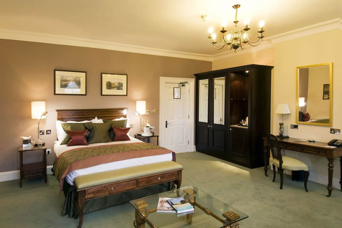 Hotellihuone, jossa on sänky, yöpöytälamput, työpöytä, tuoli, lasinen sohvapöytä ja vaatekaappi.