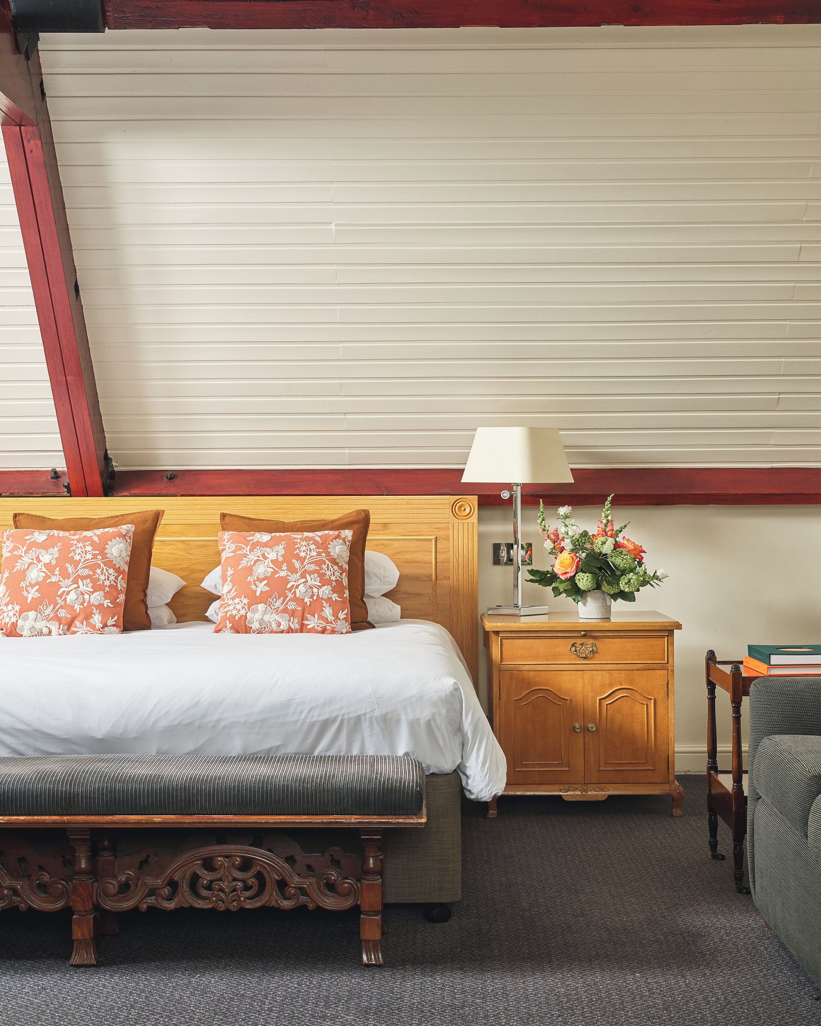 A hotel room with a bed, a wooden nightstand, a lamp, and a floral arrangement.