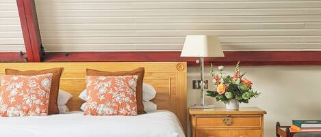 A hotel room with a bed, a wooden nightstand, a lamp, and a floral arrangement.