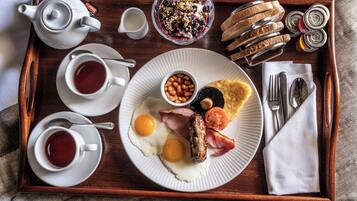 A breakfast tray with eggs, sausage, bacon, toast, jam, and a teapot.