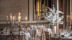 Un comedor formal con mesas dispuestas para una comida, con candelabros y centros de mesa florales.
