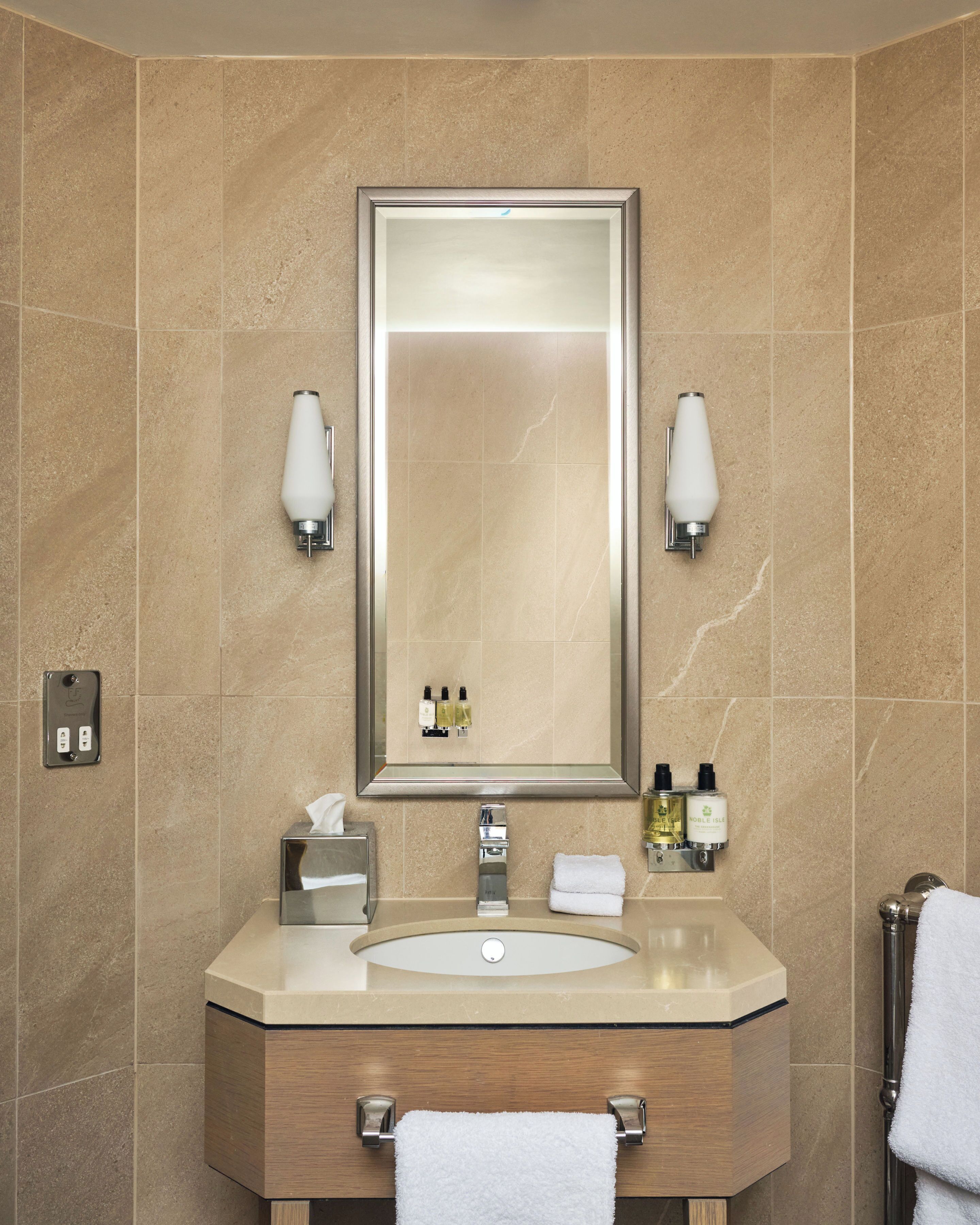 A bathroom with a large mirror, a sink, two wall-mounted lights, a towel rack, and toiletries.