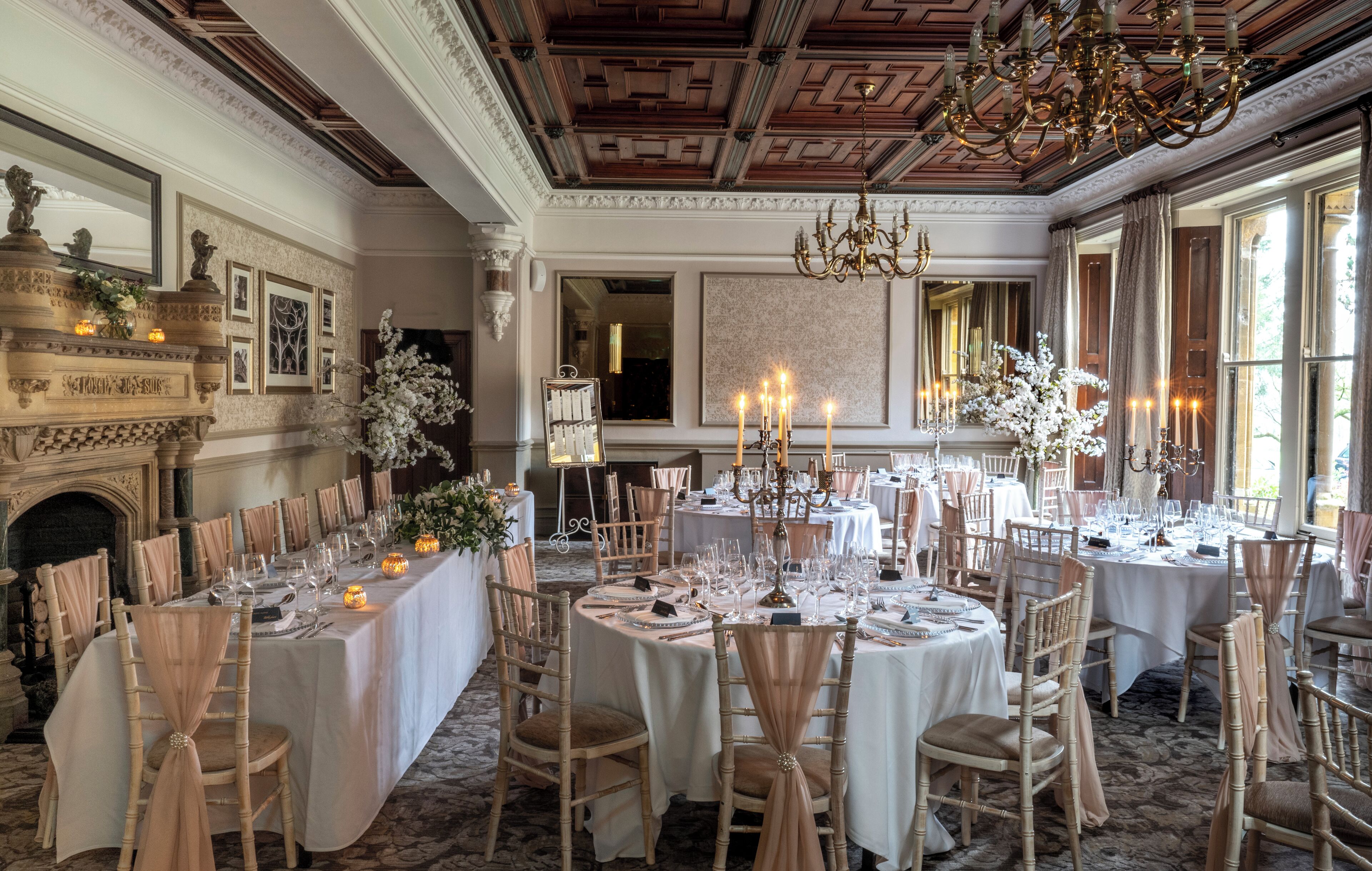 Une salle à manger formelle avec plusieurs tables rondes dressées pour un repas, de magnifiques lustres et une cheminée.