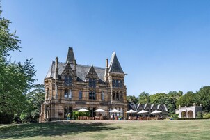Un edificio grande e histórico con múltiples torres y un amplio patio con mesas al aire libre.
