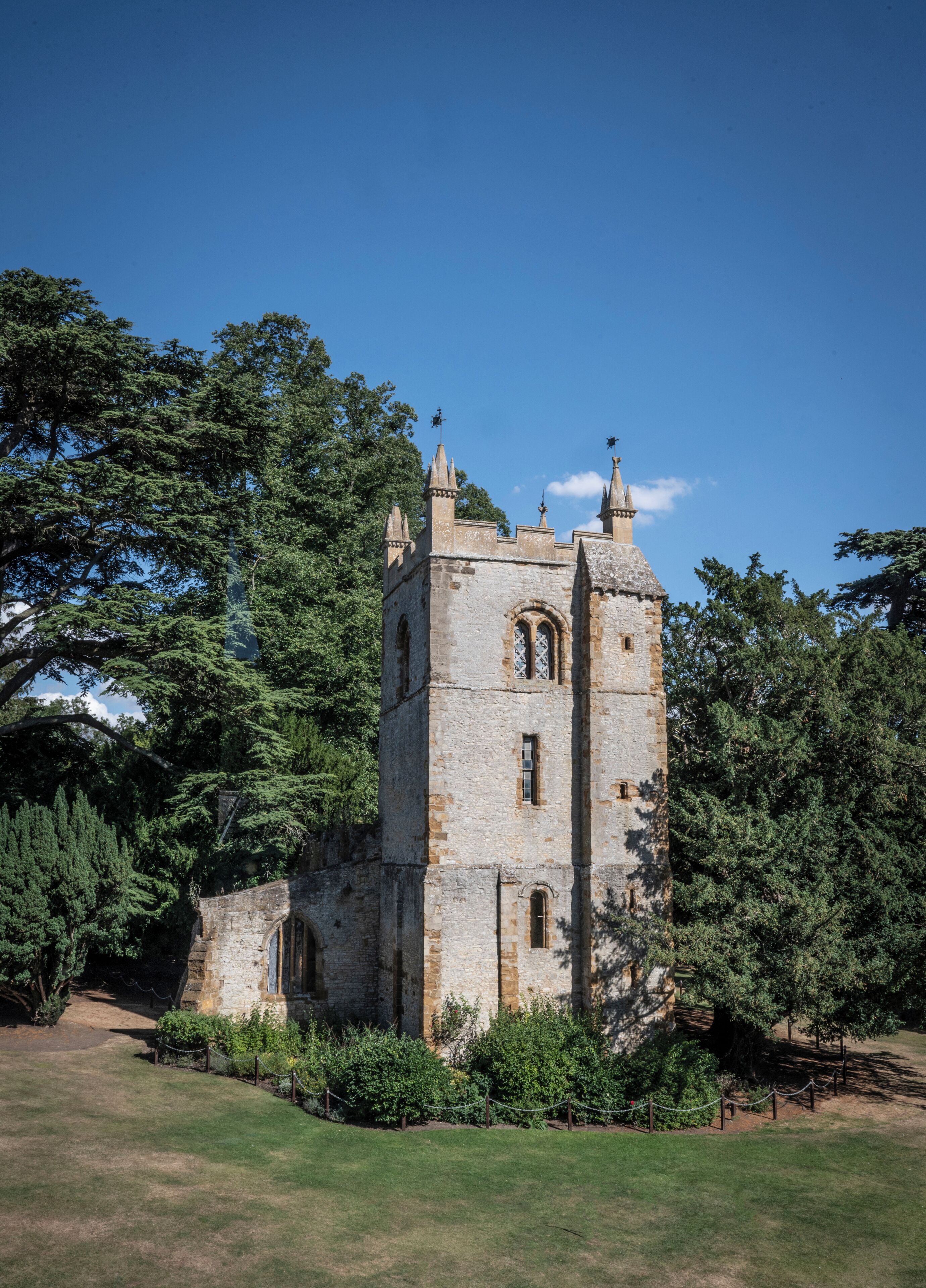 A historic stone tower with arched windows and battlements, surrounded by trees and a grassy area.