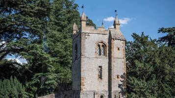A historic stone tower with arched windows and battlements, surrounded by trees and a grassy area.