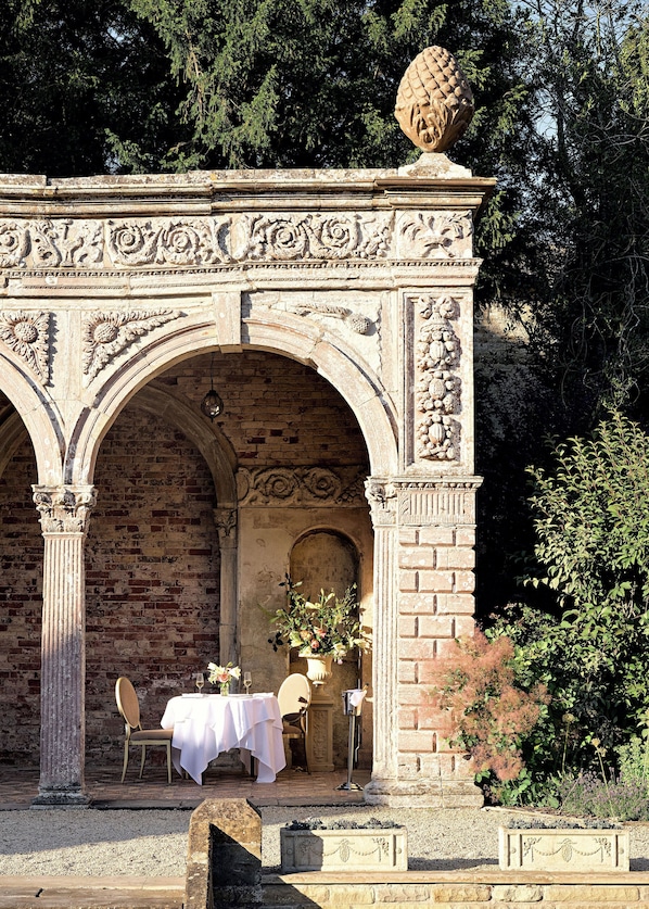 An outdoor dining area with a brick wall, stone arches, and a table set for two.