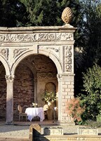 Un área de comedor al aire libre con pared de ladrillo, arcos de piedra y una mesa para dos.
