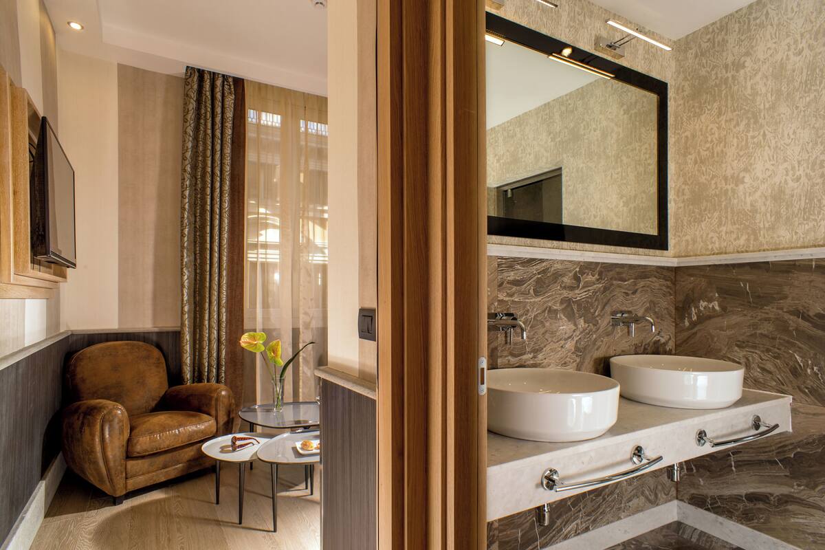 A modern bathroom with a double sink vanity, a leather armchair, and a small table with a vase.