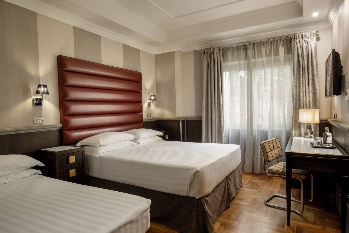 A hotel room with two beds, a desk, a chair, and a TV.