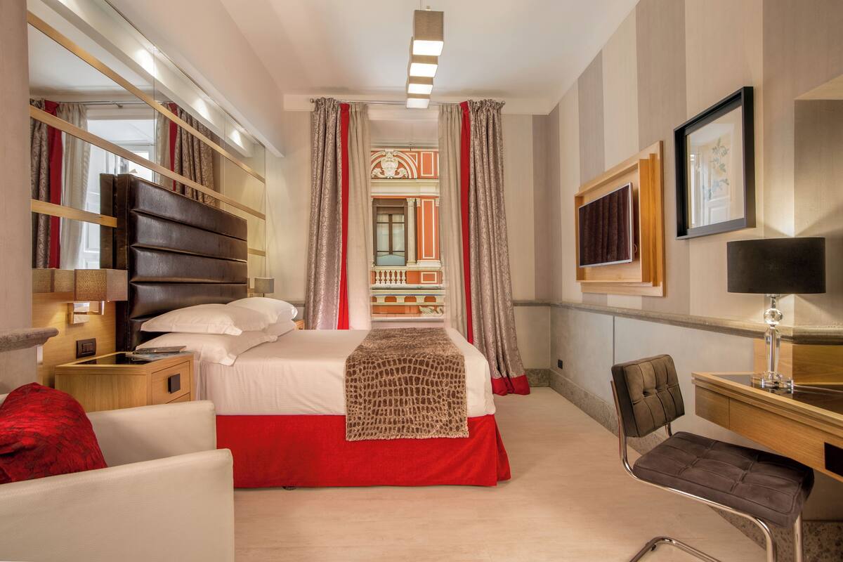 A hotel room with a bed, a desk, a chair, and a mirror.