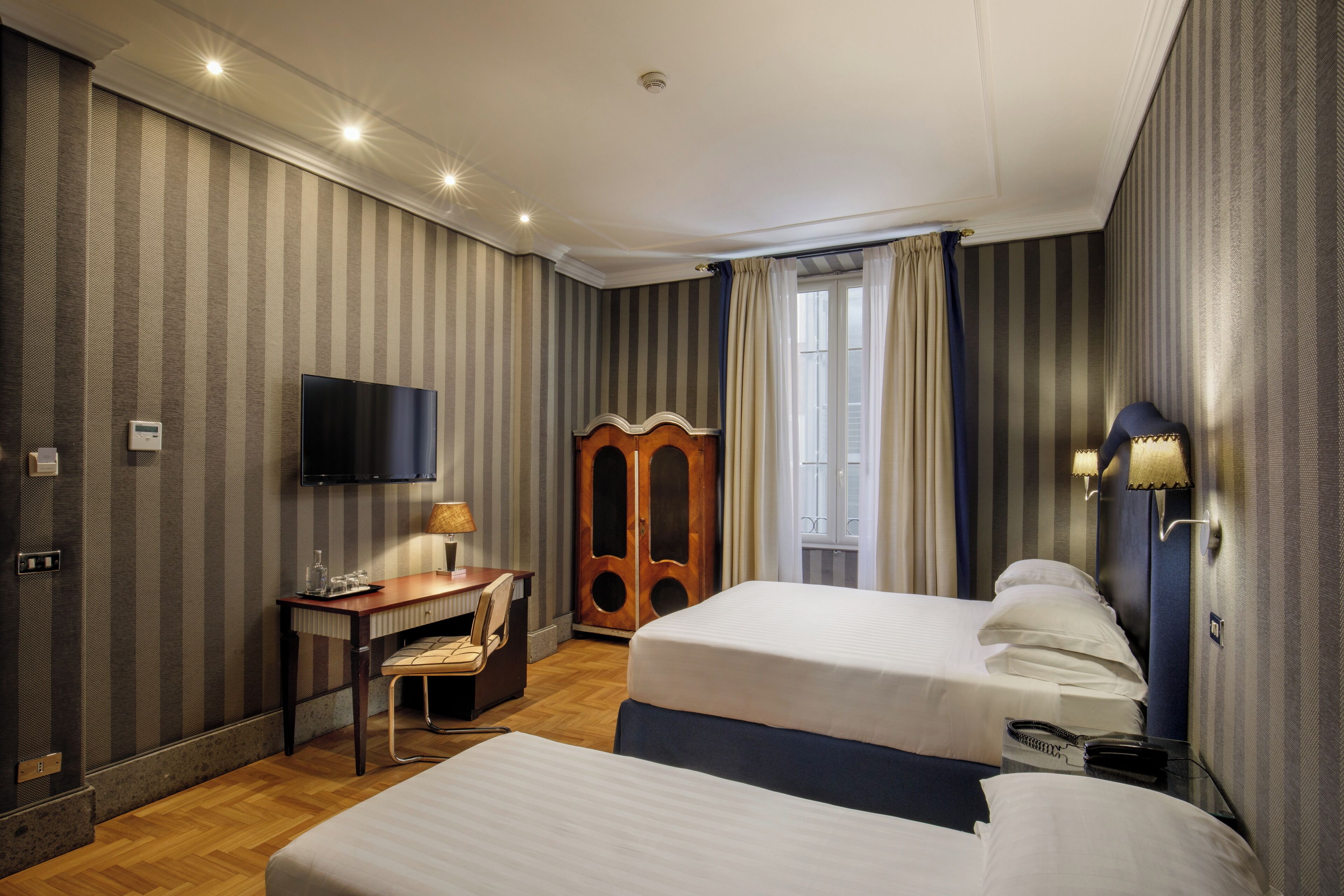 A hotel room with two beds, a desk with a chair, a television, and a wardrobe.