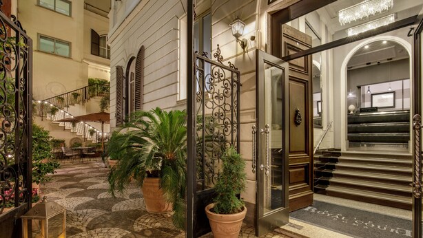 A hotel entrance with a cobblestone courtyard, a wrought iron gate, and a staircase leading to the interior. - Hotel Royal Court (Rome)