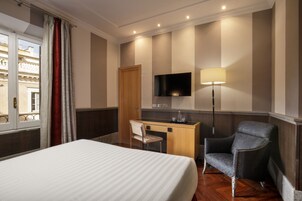 A hotel room with a bed, a desk, a chair, a TV, and a lamp.
