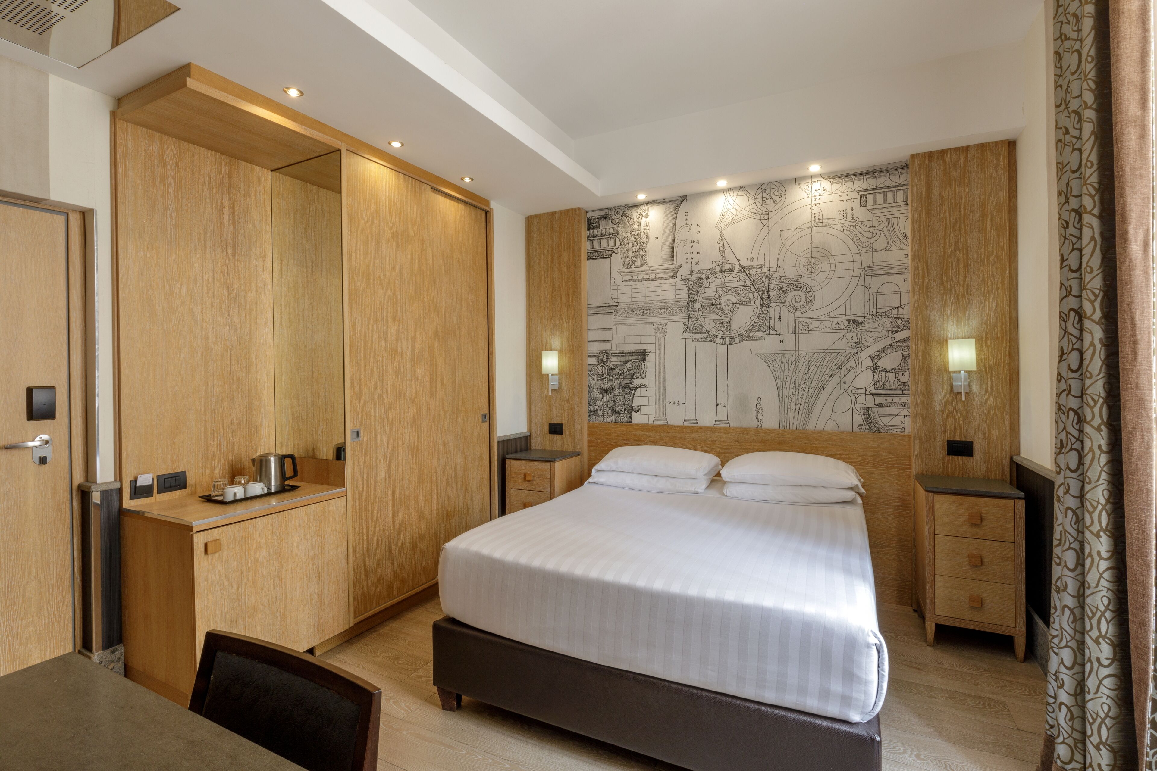 A hotel room with a large bed, wooden wardrobe, desk, and a map mural on the wall.
