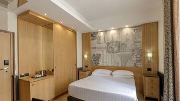 A hotel room with a large bed, wooden wardrobe, desk, and a map mural on the wall.