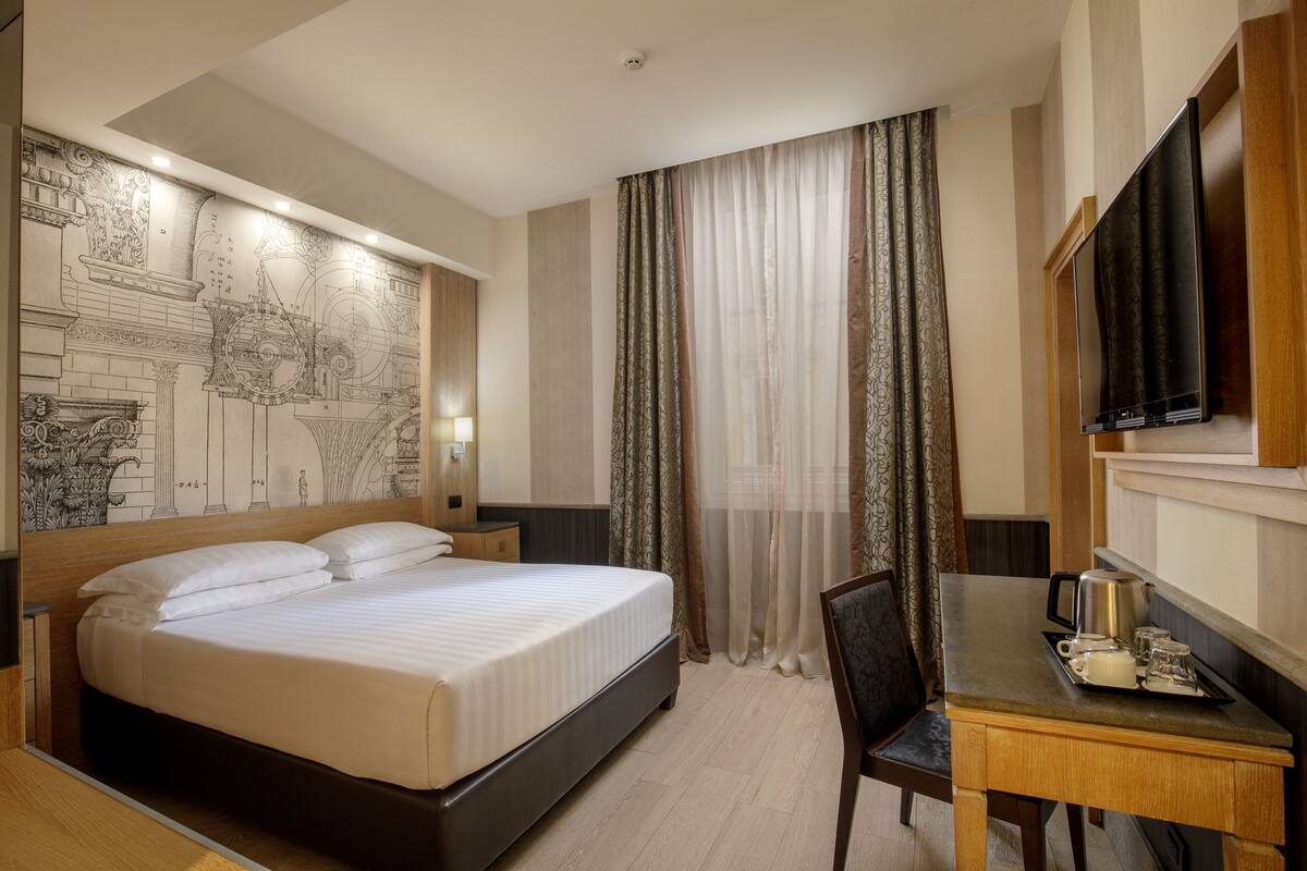 A hotel room with a large bed, a desk with a coffee maker, and a television.