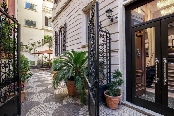 Un patio con suelo de baldosas, plantas en macetas y una reja de hierro forjado.